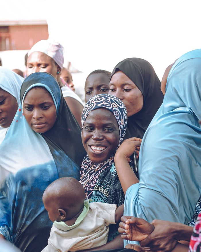 A vibrant group of women and children in colorful hijabs and traditional clothing during a daytime gathering.
